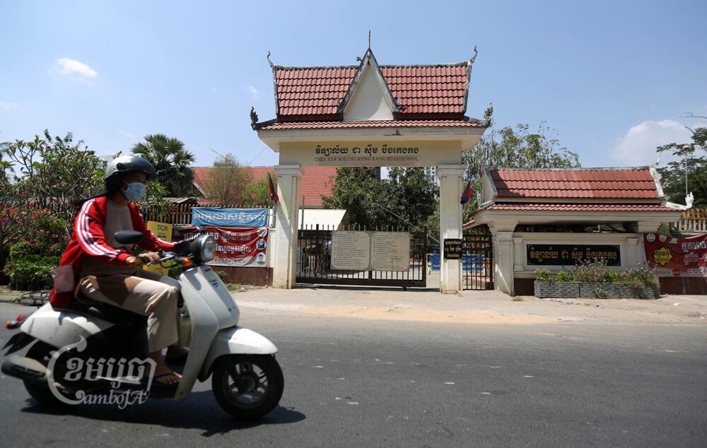 ស្រ្តីម្នាក់បើកបរកាត់សាលារៀនបិទទ្វារមួយអំឡុងពេលការរាតត្បាតជំងឺកូវីដ១៩ នៅរាជធានីភ្នំពេញ។ រូបថតកាលពីថ្ងៃទី១១ ខែមីនា ឆ្នាំ២០២១។ ខេមបូចា/ ព្រីង សំរាំង